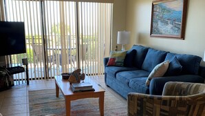 Ein Wohnzimmer mit einem blauen Sofa, einem gemusterten Sessel, einem Couchtisch und einem Fernsehgerät auf einem Lowboard.