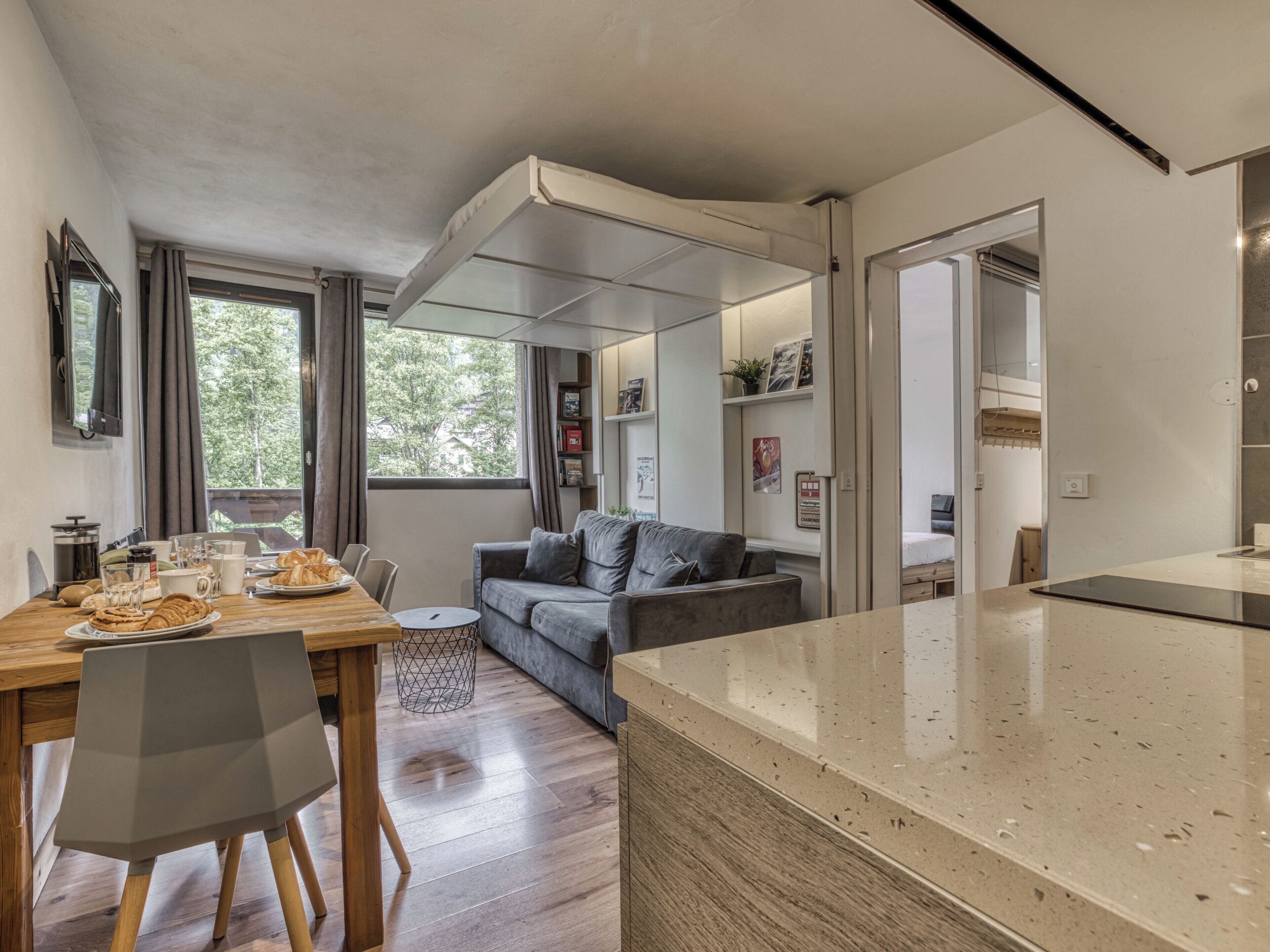 Una cocina moderna con una mesa de comedor de madera, un sofá gris y un amplio ventanal.