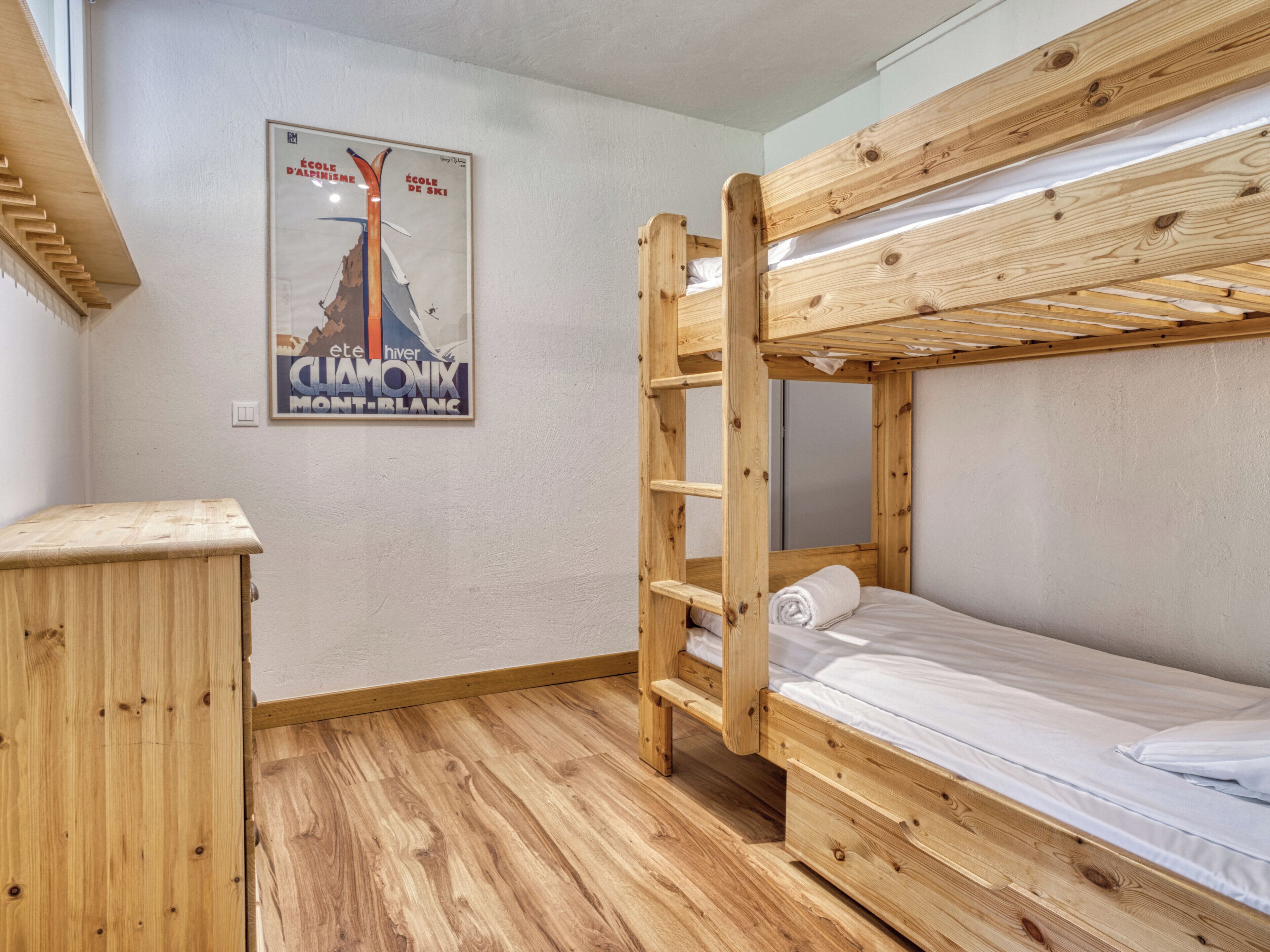 A bunk bed room with a wooden ladder, a small wooden dresser, and a poster on the wall.