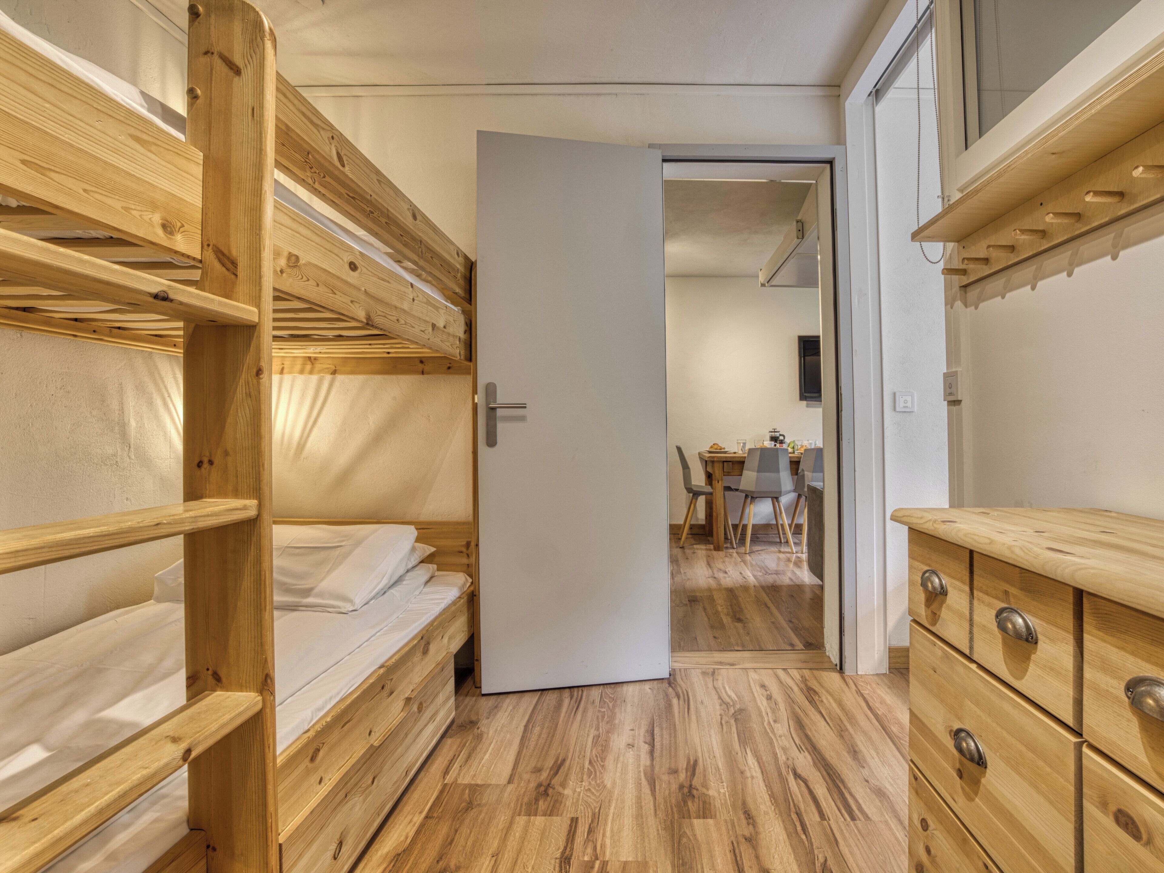 A room with bunk beds, a wooden dresser, and a dining area with chairs and a table.