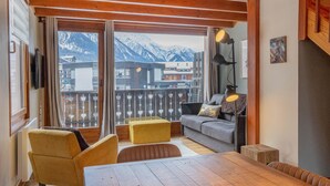 Une pièce chaleureuse avec un plafond en bois, un balcon offrant une vue sur les montagnes, un canapé, une table et une lampe.