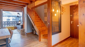 Un escalier en bois agrémenté d’un motif géométrique sur le mur, une porte en bois et une vue sur un balcon avec une chaîne de montagnes en arrière-plan.