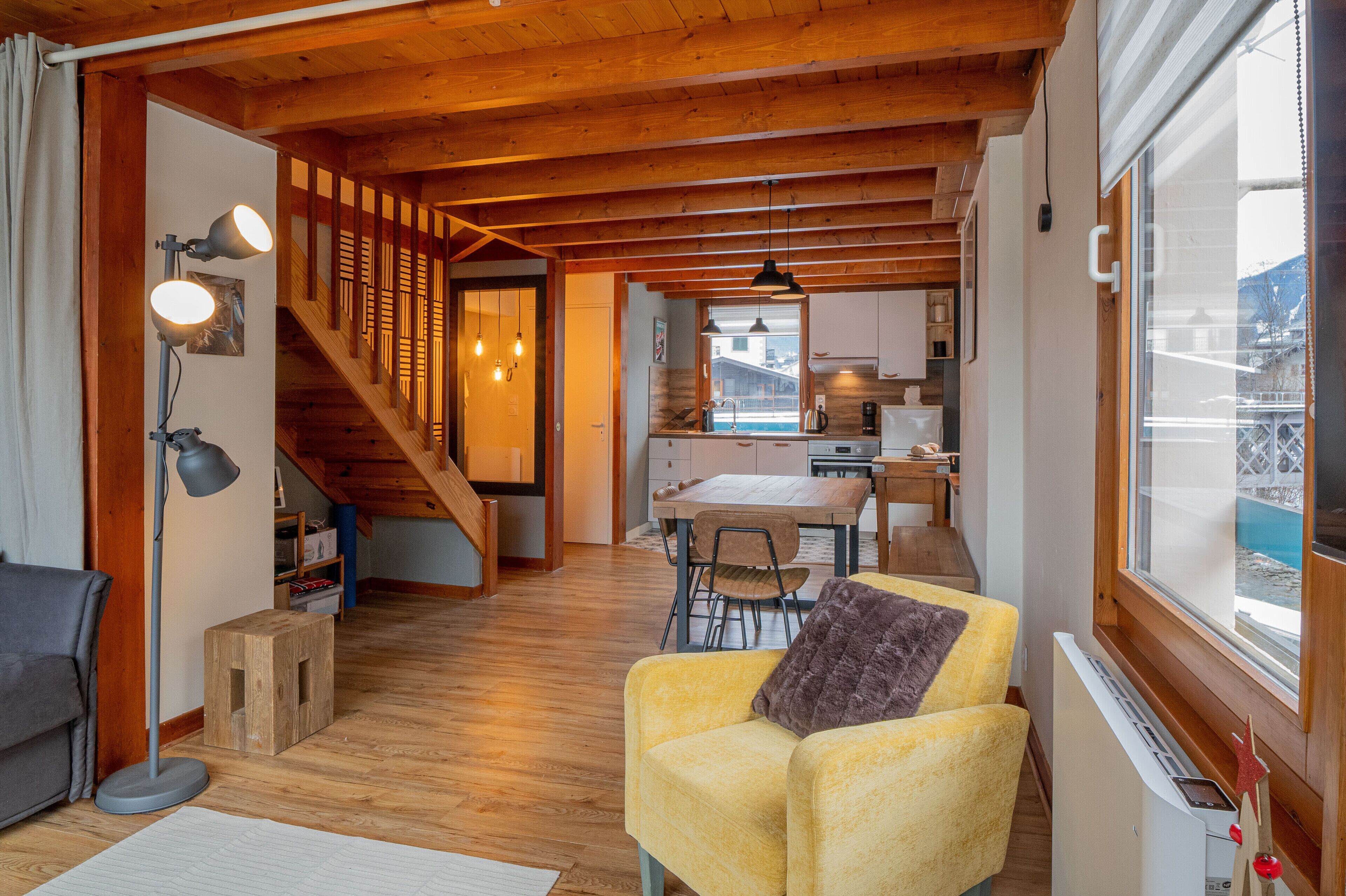 Un salon chaleureux avec un plafond en bois, un escalier, un coin repas et une cuisine.