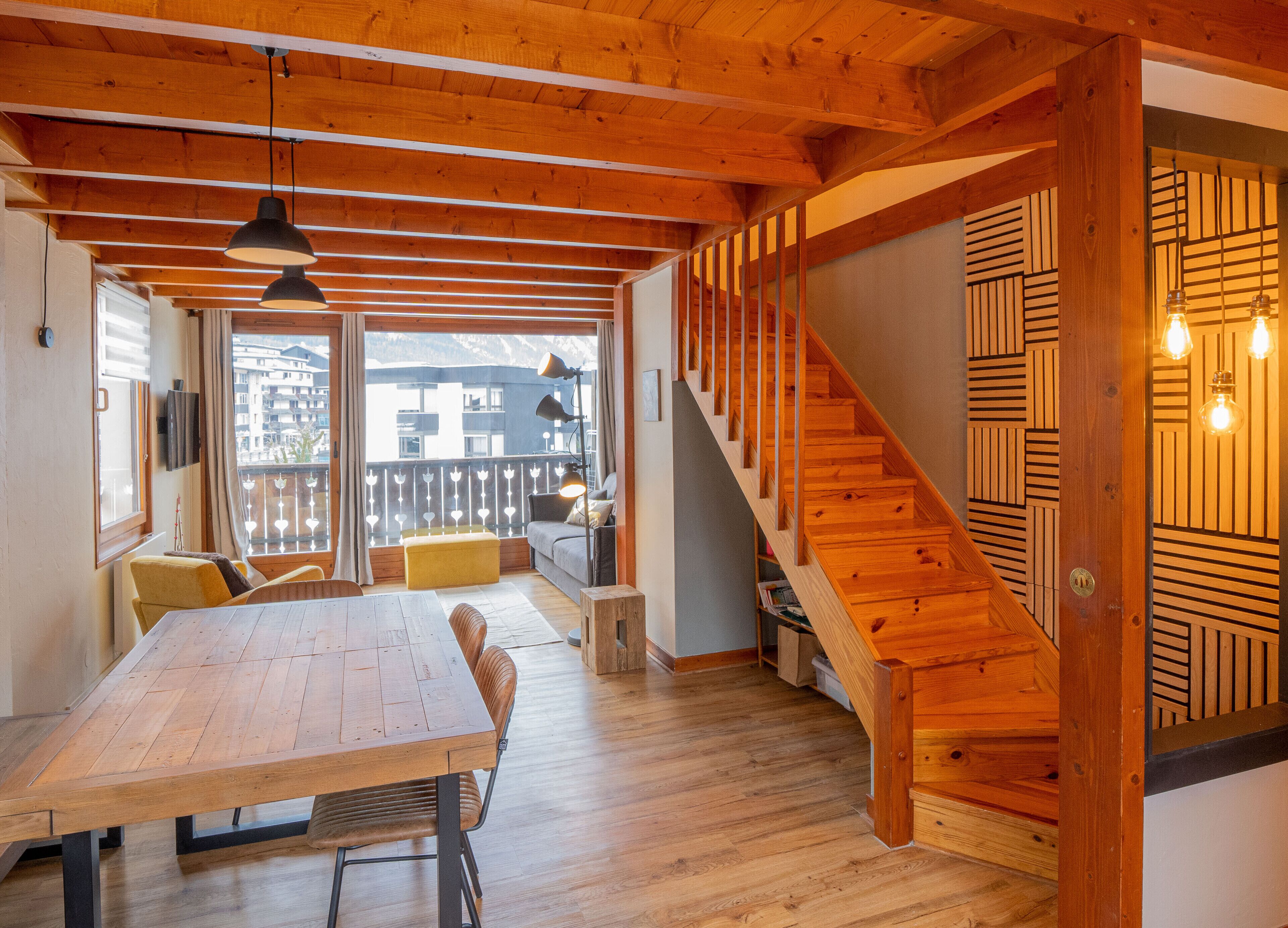 A wooden interior with a dining area, sofa, and staircase.