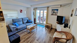 A living room with a grey sofa, a wooden coffee table, a wicker chair, and a television. - Amazing Terrace Costa da Caparica (Costa da Caparica)