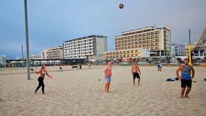 A beach with people playing volleyball, a large building in the background, and a crane. - Amazing Terrace Costa da Caparica (Costa da Caparica)