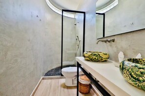 Een moderne badkamer met toilet, douche en wastafel met decoratieve kommen.