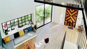 A spacious living area with a high ceiling, a staircase, and a large window overlooking greenery. - Casa Búho I Unique & Spacious 4Br Villa 10 people (Tulum)