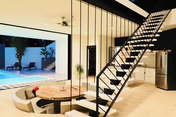 Een modern interieur met een wenteltrap, uitzicht op een zwembad en een eetgedeelte met een ronde tafel.