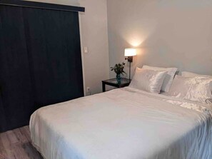 A bedroom with a bed, a nightstand, a lamp, and a dark-colored wardrobe.