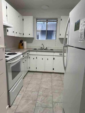 Cocina compacta con armarios blancos, estufa, lavaplatos y refrigerador.