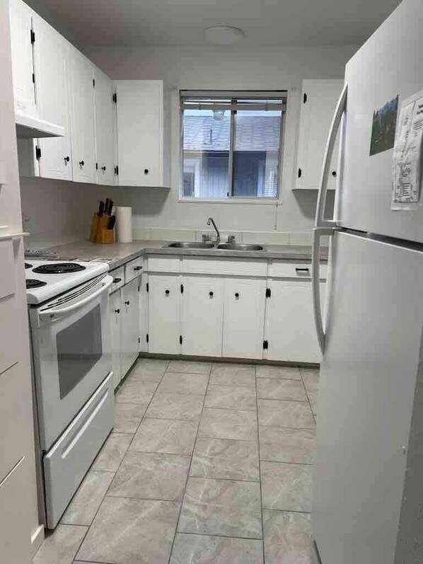 A compact kitchen with white cabinets, a stove, a sink, and a refrigerator. - Tahsis Home on River's Edge (Tahsis)