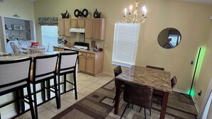 A dining area with a table and chairs, a kitchen in the background, and a chandelier. - Near Disney & Universal Pool + Spa Family 4BR Private Pool, Spa Fenced Yard (Kissimmee)