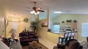 A living room with a sofa, armchair, coffee table, and a dining area with chairs and a kitchen in the background. - Near Disney & Universal Pool + Spa Family 4BR Private Pool, Spa Fenced Yard (Kissimmee)