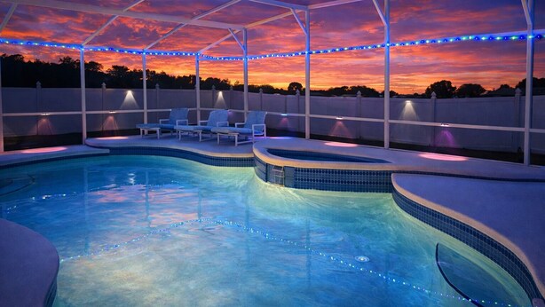 A swimming pool with a covered area, lounge chairs, and string lights. - Near Disney & Universal Pool + Spa Family 4BR Private Pool, Spa Fenced Yard (Kissimmee)