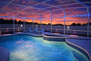 A swimming pool with a covered area, lounge chairs, and string lights.