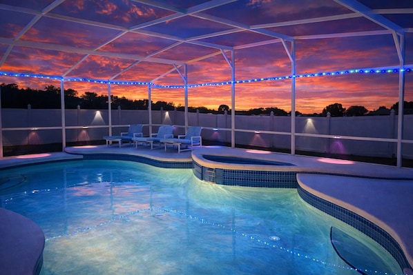 A swimming pool with a covered area, lounge chairs, and string lights.