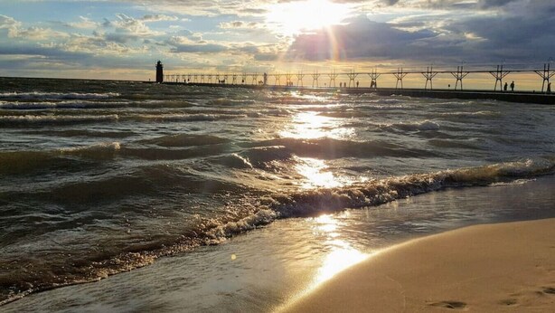 A beach with waves, a pier, and a lighthouse.