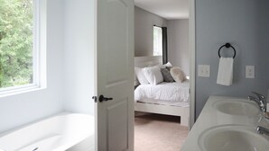A bedroom with a bed, a window, and a bathroom with two sinks.