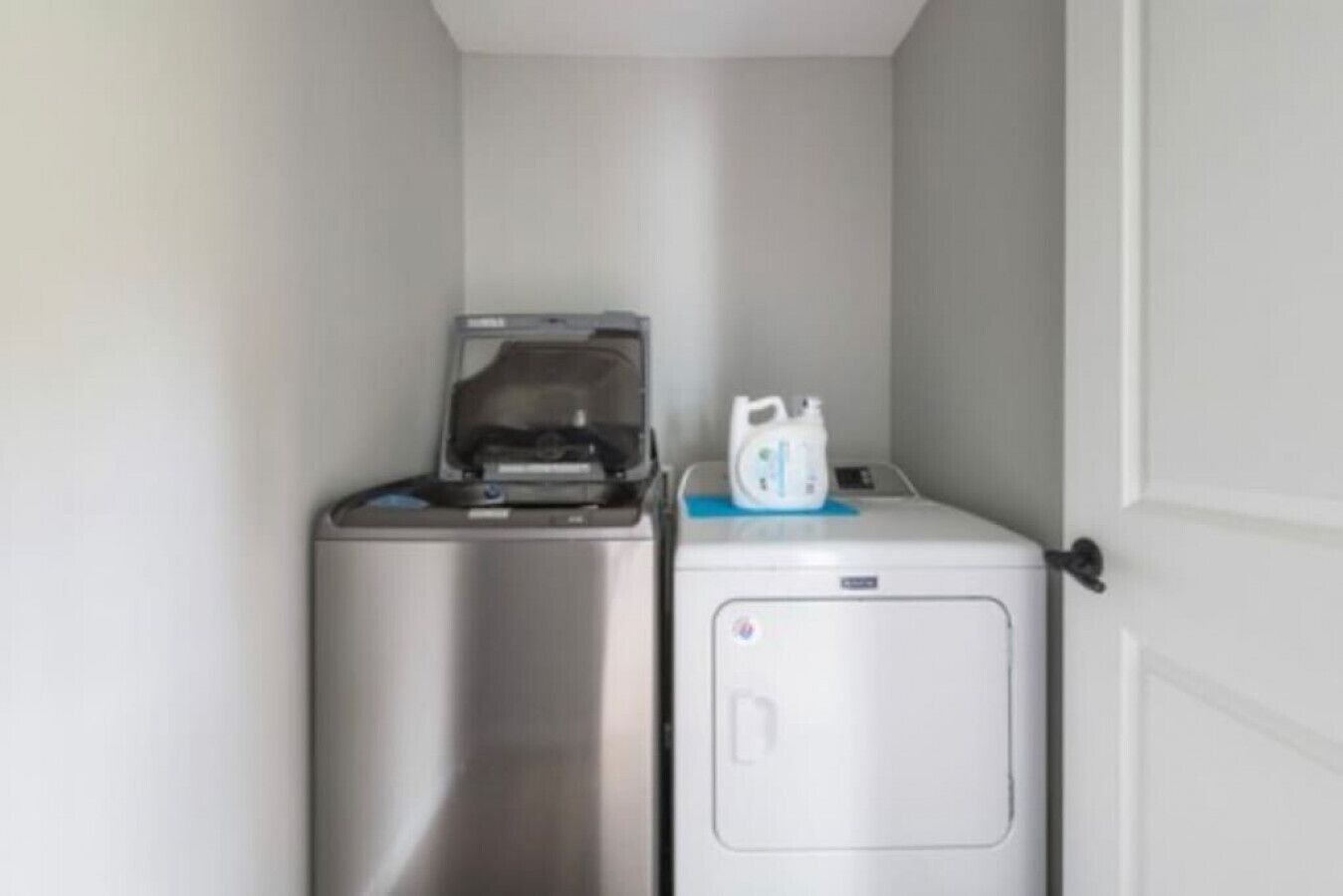 Een kleine wasruimte met een wasmachine van roestvrij staal en een witte droger.
