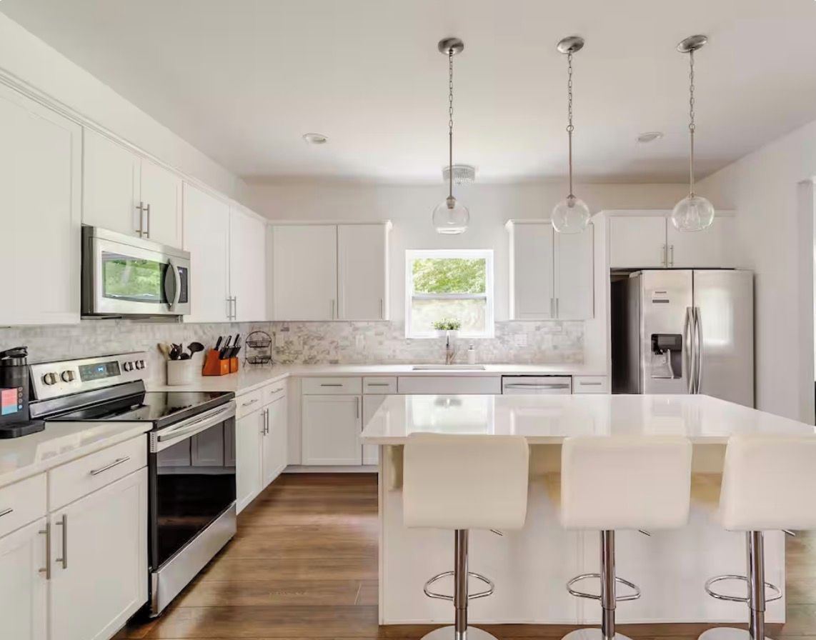A modern kitchen with white cabinetry, stainless steel appliances, a central island with bar stools, and pendant lighting.