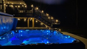 A hot tub with blue lighting, a deck with lights, and a building in the background.