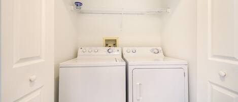 A laundry room with two white front-loading washing machines and a shelf above them.