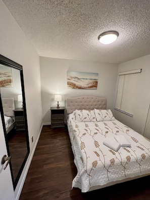 A bedroom with a bed, a nightstand, a lamp, a painting on the wall, and a window with blinds. - Grand Family Deluxe 3BD Condo Near Disney Universal 22 (Kissimmee)