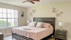 Un dormitorio con cama, mesita de noche, ventilador de techo y ventana.
