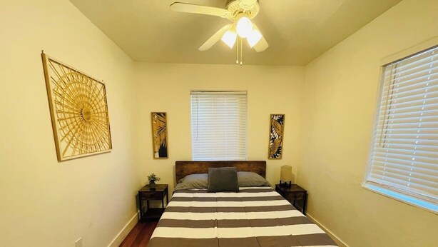 A bedroom with a bed, a ceiling fan, two bedside tables, and a window with blinds.