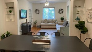A modern living room with a dining area, a television, decorative wall art, and a ceiling fan.