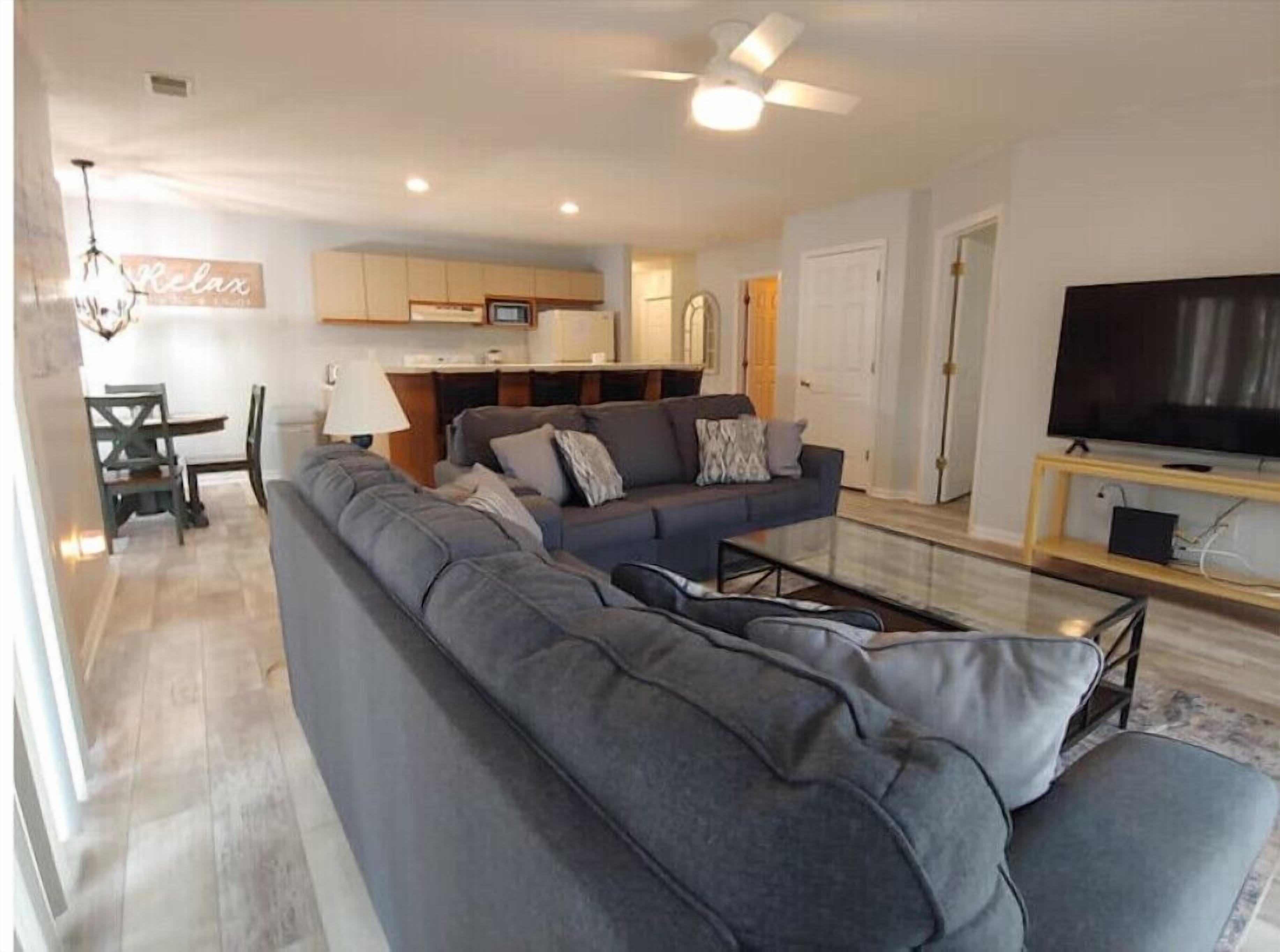 Una sala de estar moderna con un sofá seccional gris grande, un televisor de pantalla plana y un comedor con mesa y sillas.