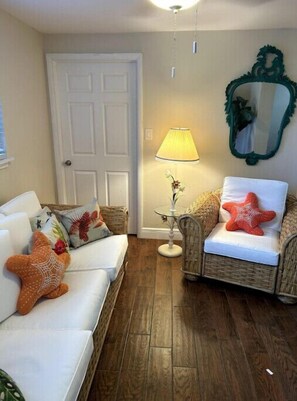 A cozy living room with a white sofa, a wicker chair, and a small table with a lamp.