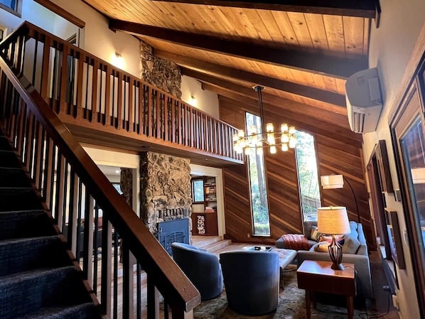 A spacious living area with a wooden staircase, stone pillar, and a large window providing natural light.