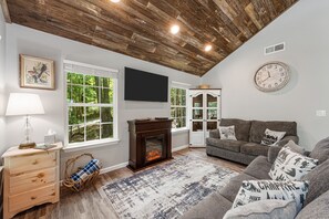 Cozy living room with a fireplace, comfortable sofa, and large windows offering a view of the outdoors.