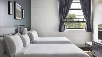 Une chambre avec deux lits, une fenêtre avec des rideaux, une commode et des tableaux encadrés accrochés au mur.