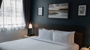 A hotel room with a large bed, a nightstand with a lamp, and a view of a building through the window.
