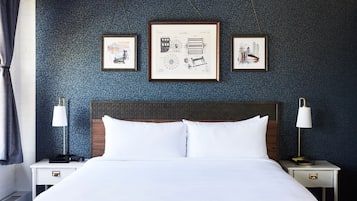 A neatly made bed with white linens, two bedside tables with lamps, and three framed pictures on the wall.