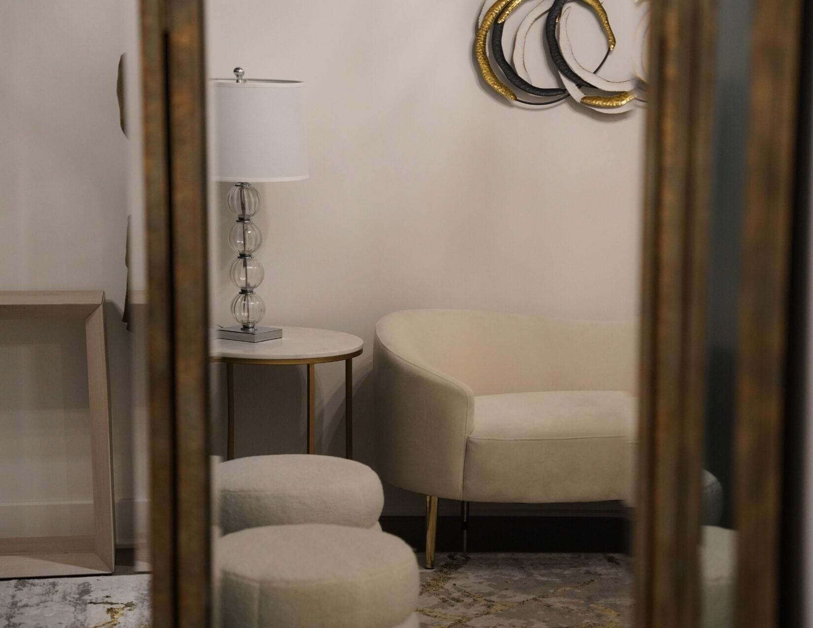 A room with a round table, a lamp, a chair, and a decorative wall piece.