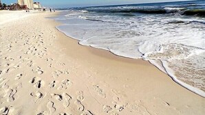 A sandy beach with footprints, waves, and buildings in the background. - Spacious 2BR condo in a premier beachfront resort. Your perfect getaway! (Panama City Beach)