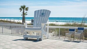 A beachside deck with a white Adirondack chair, a lounge chair, and a railing overlooking the ocean. - Spacious 2BR condo in a premier beachfront resort. Your perfect getaway! (Panama City Beach)