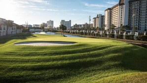 A golf course with a pond, surrounded by modern buildings and a clear sky. - Spacious 2BR condo in a premier beachfront resort. Your perfect getaway! (Panama City Beach)