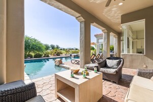 A poolside area with a stone patio, wicker furniture, and a wooden table with drinks.