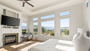 A bedroom with a large bed, a TV, a fireplace, and multiple windows offering a mountain view. - Multi-Million Dollar PGA West 4BR/5BA Pool/Spa (La Quinta)