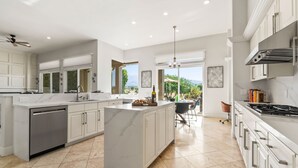 A modern kitchen with a central island, white cabinetry, and a view to the outdoors. - Multi-Million Dollar PGA West 4BR/5BA Pool/Spa (La Quinta)
