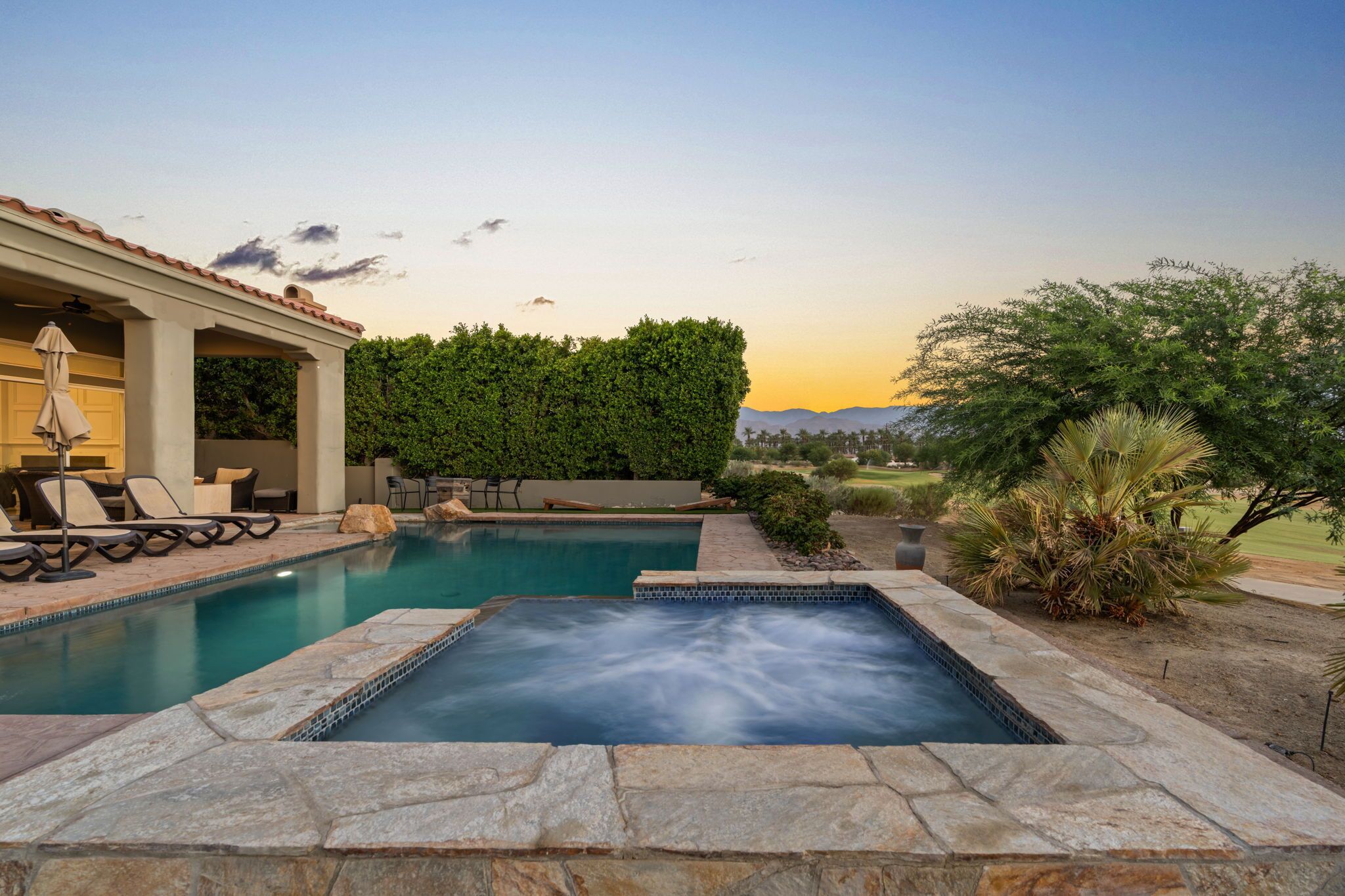 A swimming pool with a hot tub, lounge chairs, and a covered patio area.