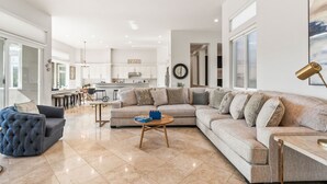 A spacious living room with a large sectional sofa, a tufted armchair, and a coffee table. The room has a high ceiling with exposed wooden beams and recessed lighting. - Multi-Million Dollar PGA West 4BR/5BA Pool/Spa (La Quinta)