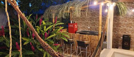 Una silla hamaca, una mesa de comedor y sillas en un entorno exterior con una pared de piedra y techo de madera.