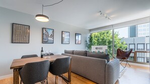 Una sala de estar moderna con una mesa de comedor de madera, sofá gris y un balcón con un letrero que dice 'GUEST READY'.