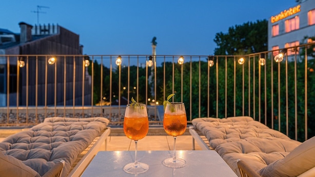 Una terraza con dos zonas de estar acolchadas, una mesa y dos vasos de una bebida con guarnición.